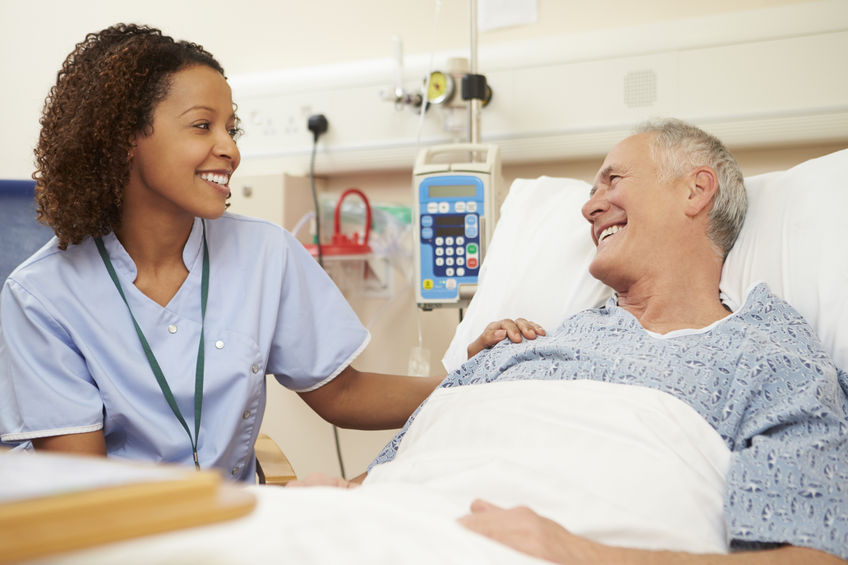 nurse sitting by male patient's bed in hospital